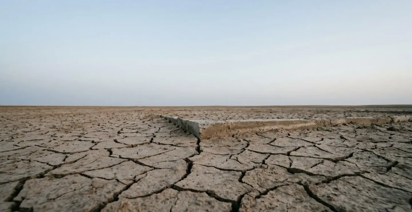 Paysage minimaliste montrant un terrain sec et fissuré sous un ciel immense évoquant les risques de sécheresse pour les constructions
